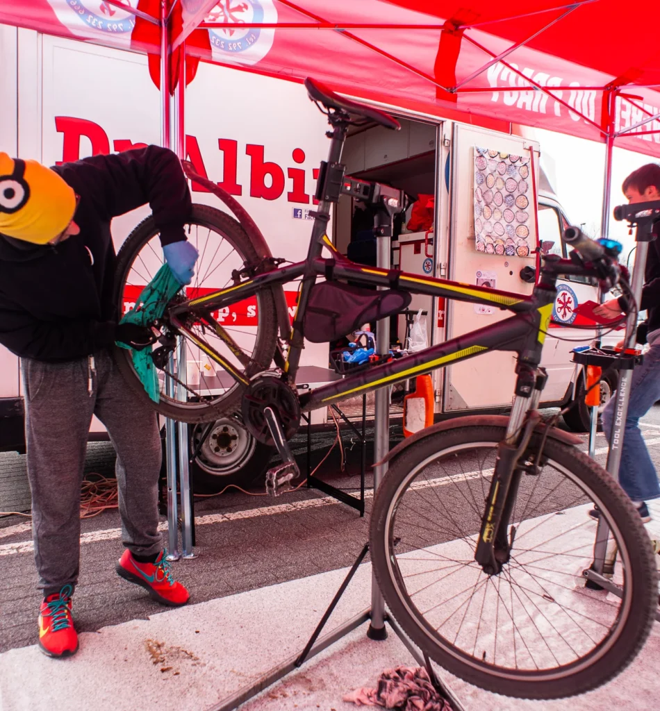 Na zdjęciu mechanik rowerowy czyści napęd rowerowy, dbając o precyzję i jakość serwisu. W tle widoczna jest karetka rowerowa Dr Albin, symbol naszego mobilnego serwisu rowerowego. Pod rowerem znajduje się mata zabezpieczająca podłogę przed smarami, podkreślająca nasze ekologiczne podejście i dbałość o czystość.